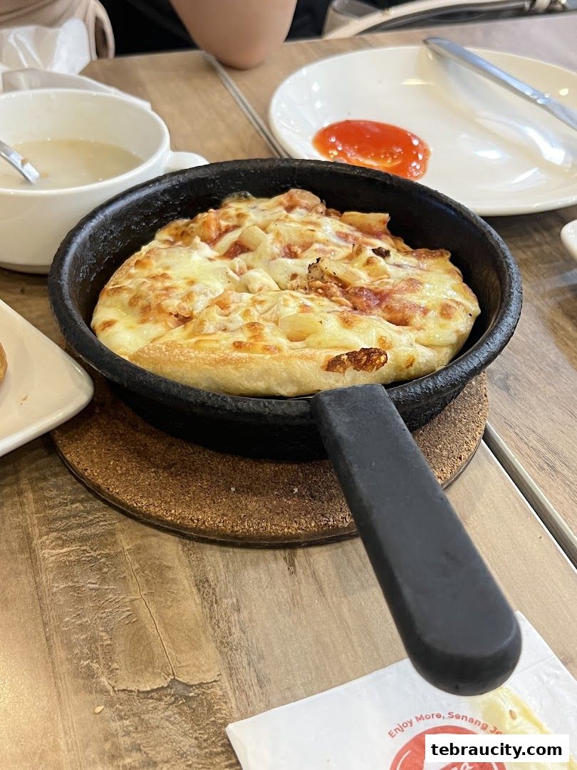A close-up of a hot pan pizza with melted cheese and toppings, served with a side of soup.