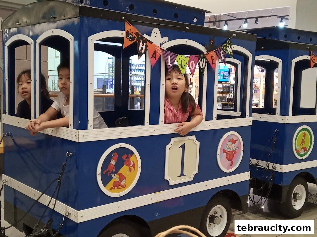 Children enjoy a festive blue train ride decorated with Halloween banners and cartoon characters.
