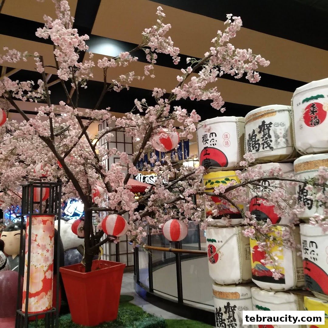 A decorative display featuring a cherry blossom tree with lanterns and stacked barrels.