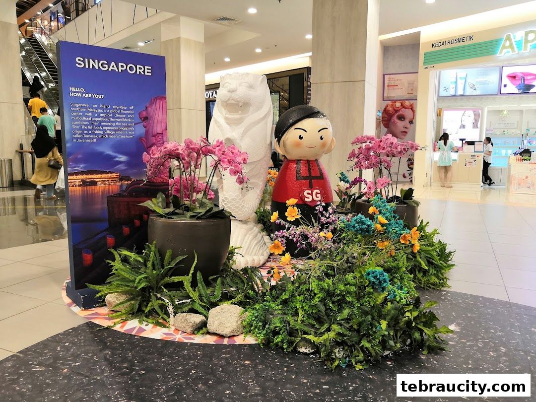 A Singapore-themed display with a Merlion statue, a cartoon figure, and floral arrangements in a mall.