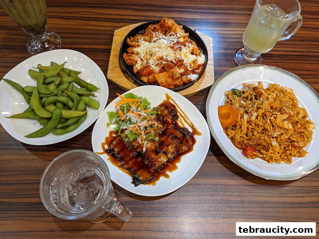 A table laden with delicious Asian dishes, including noodles, chicken, and edamame.