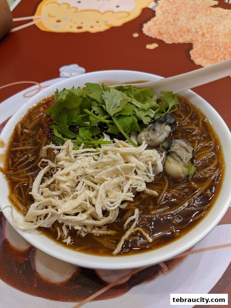A bowl of oyster vermicelli soup topped with shredded chicken and cilantro.