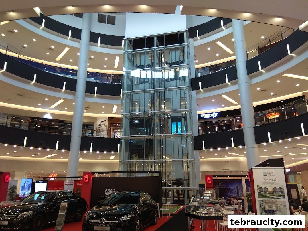 Interior view of a multi-level shopping mall with an atrium, glass elevator, and various shops.