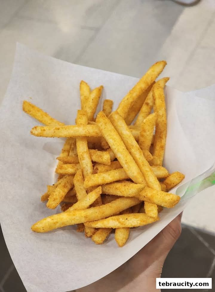 A hand holding a paper cone filled with seasoned french fries.