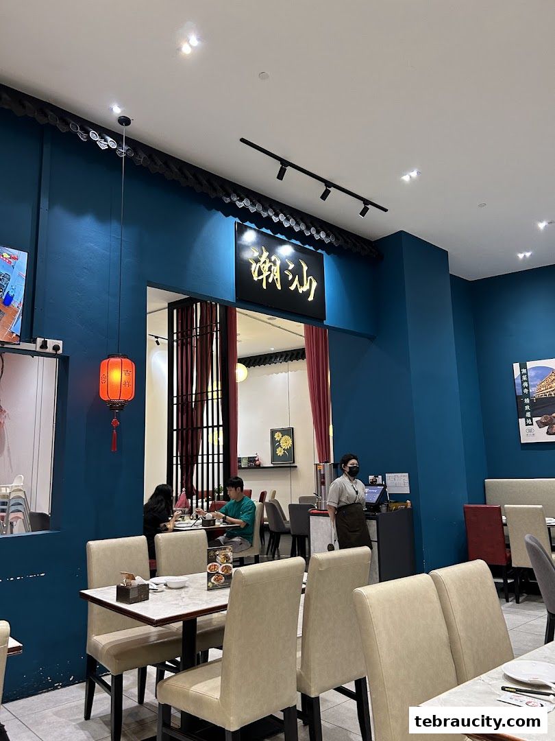 Interior of a restaurant with blue walls, tables, chairs, and a staff member.
