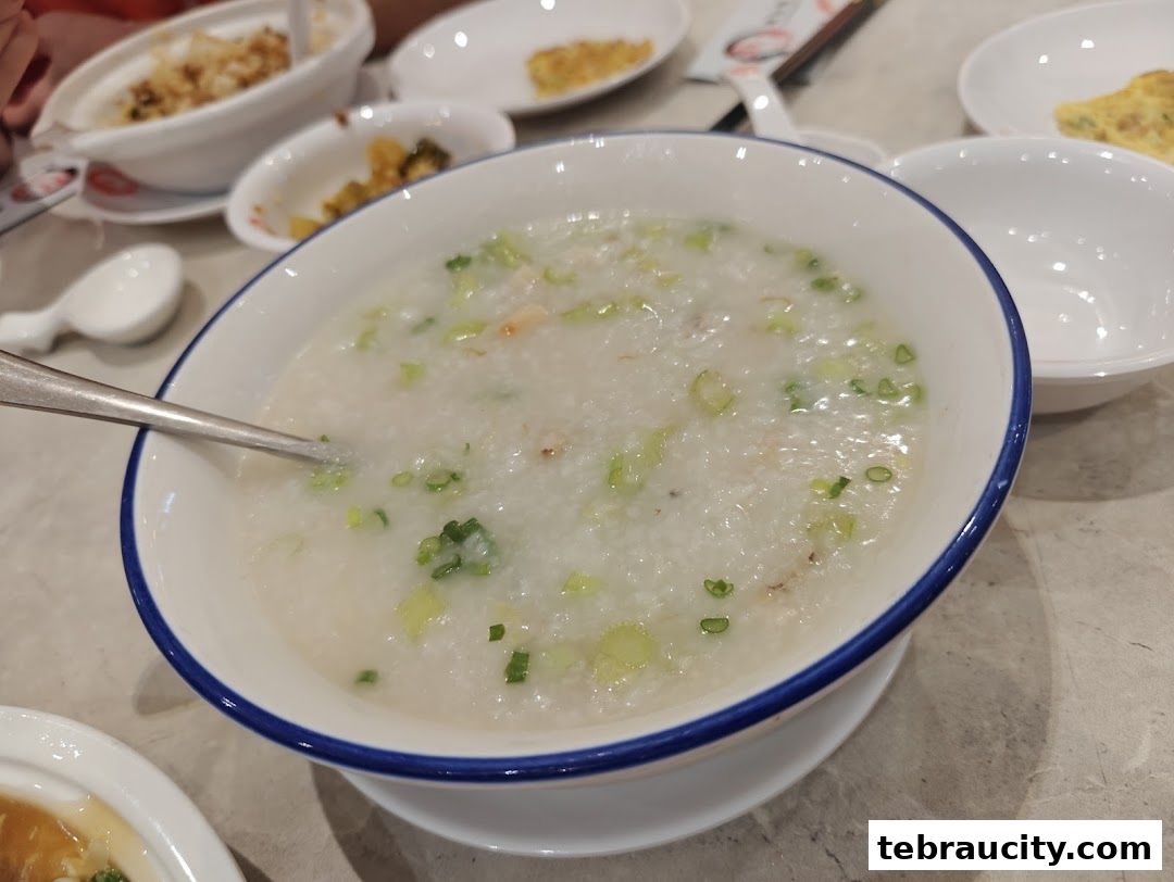 A close-up of a bowl of congee with chopped scallions and a spoon.
