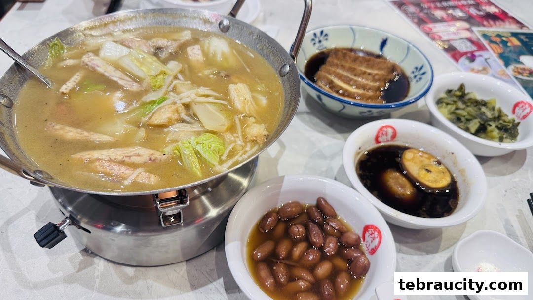 A steaming pot of soup with various ingredients, served with side dishes.