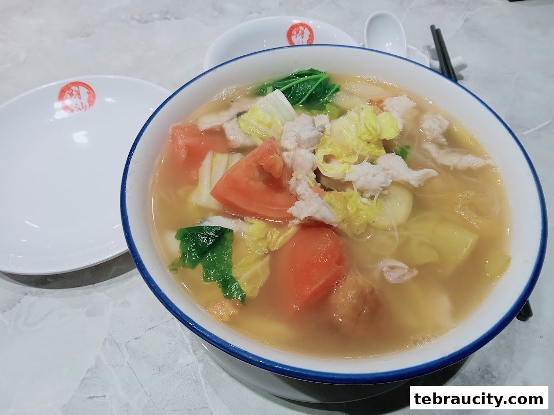 A steaming bowl of noodle soup with meat, vegetables, and tomatoes.