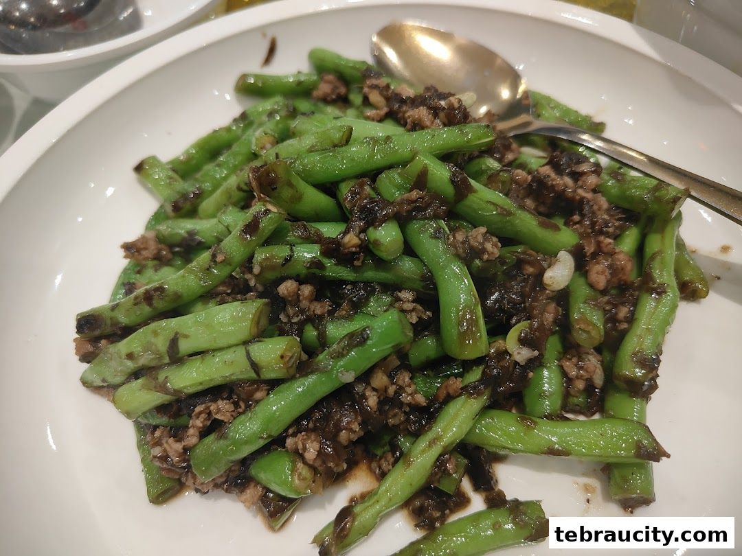 A close-up shot of stir-fried green beans with minced meat on a white plate.