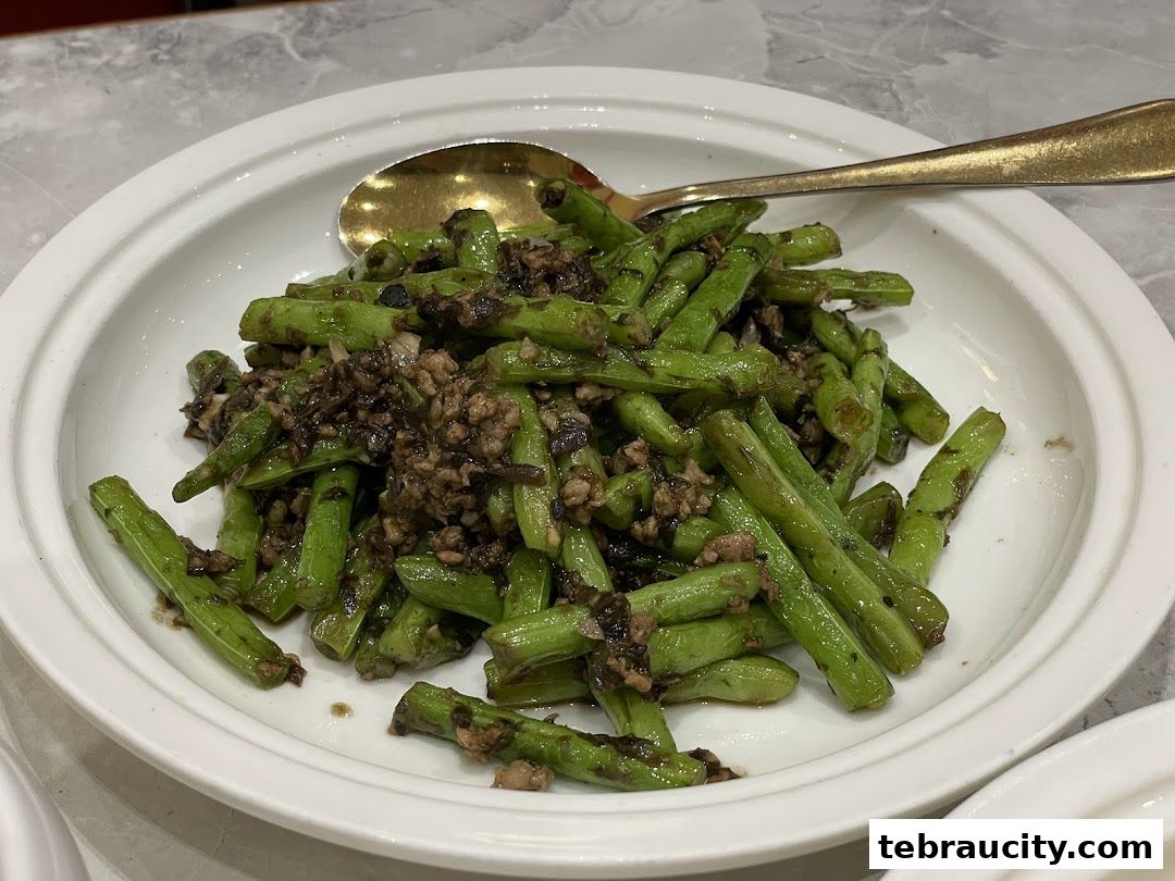 A close-up shot of a white plate filled with stir-fried green beans and minced meat.