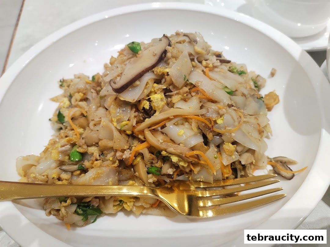 A close-up shot of a plate of stir-fried noodles with mushrooms, egg, and vegetables.