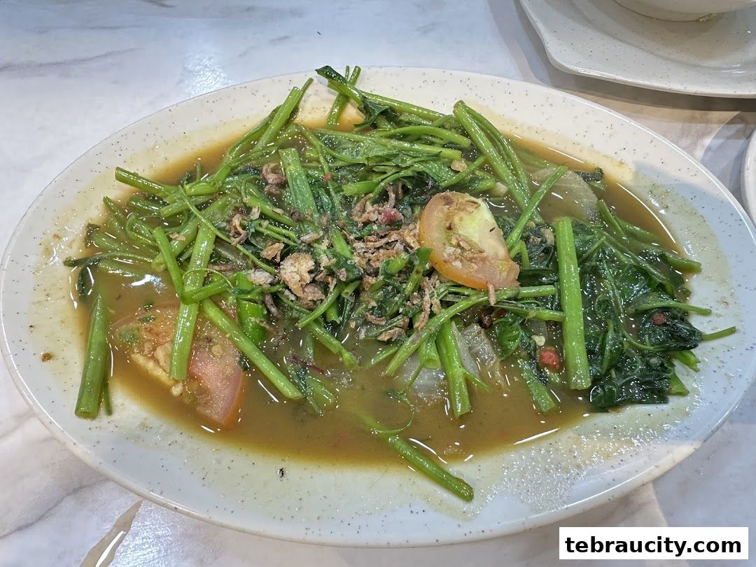 A plate of stir-fried water spinach with tomatoes and fried shallots in a savory sauce.