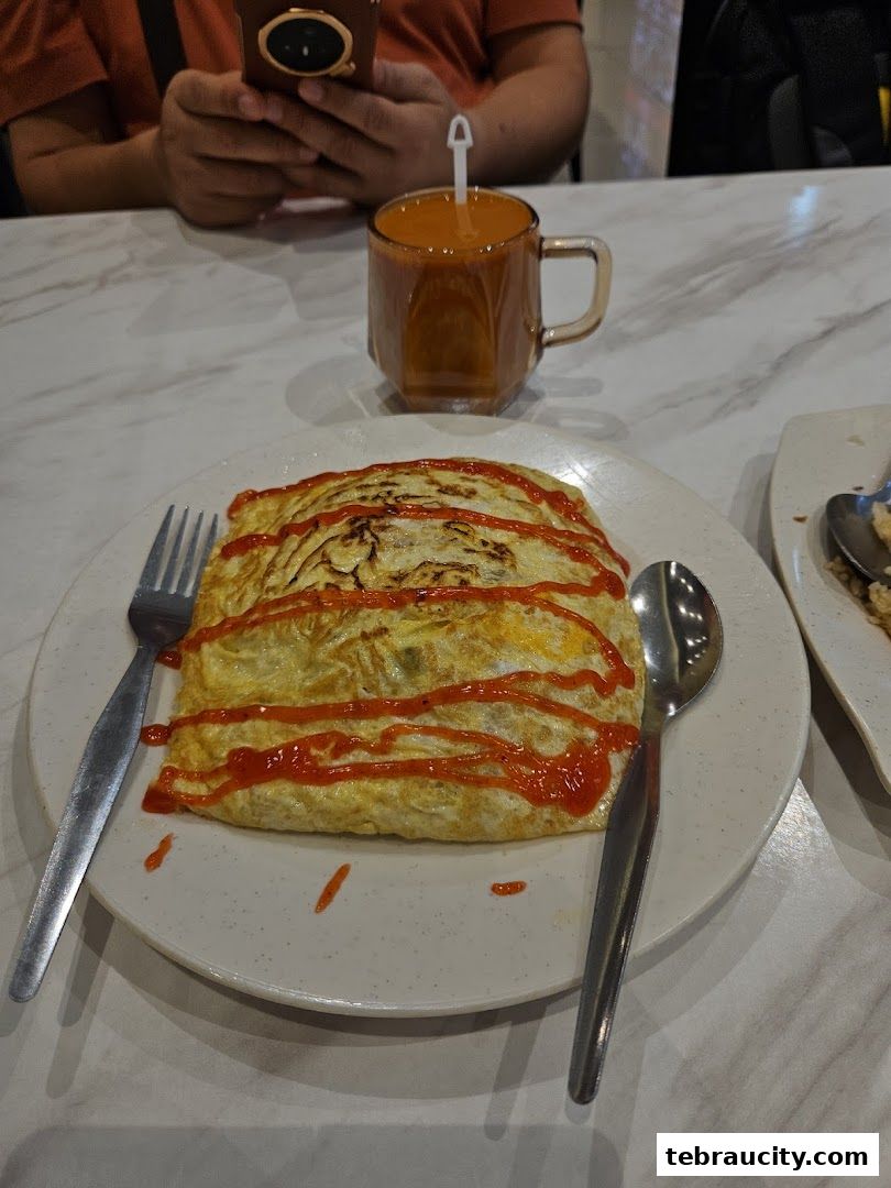 A plate of omelette rice drizzled with ketchup, served with a drink and cutlery.