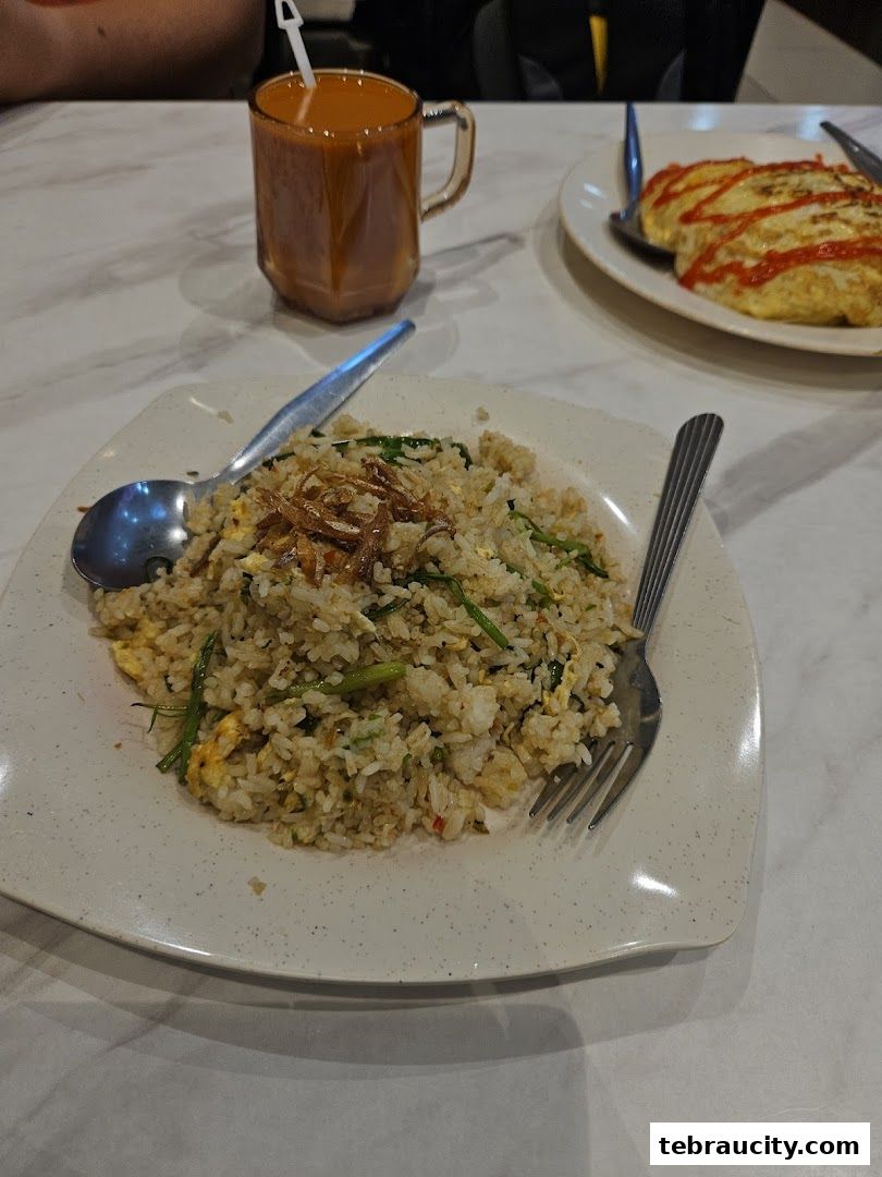 A plate of fried rice with a drink and another dish in the background.