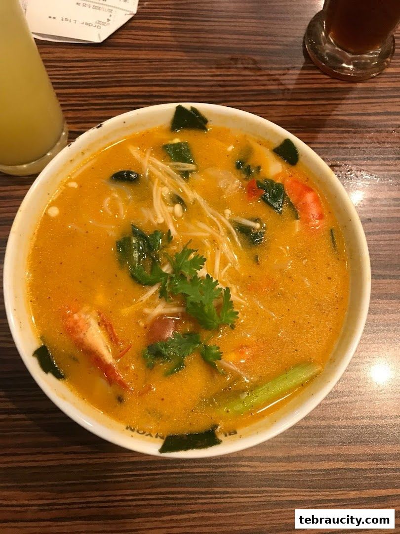 A close-up of a steaming bowl of Tom Yum soup with shrimp and mushrooms.