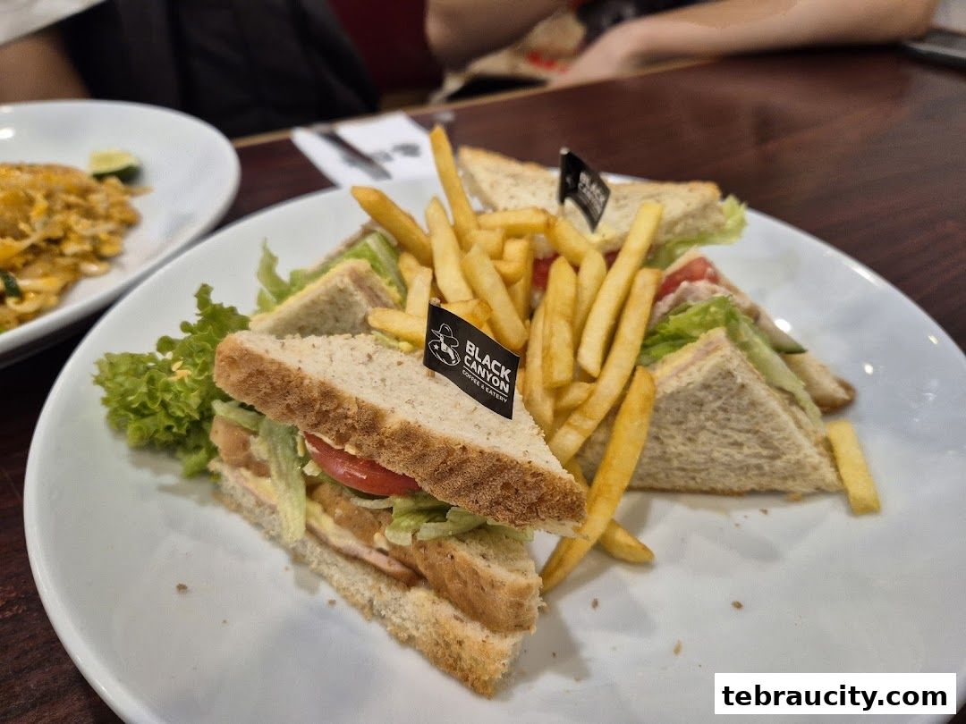 A plate of sandwiches and french fries, with a side of noodles, at a restaurant.