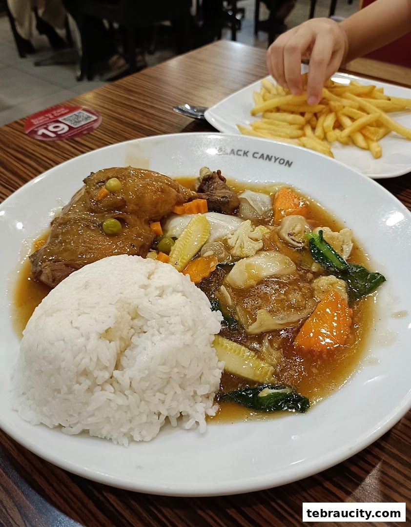 A plate of rice with chicken and vegetables, and a side of french fries.