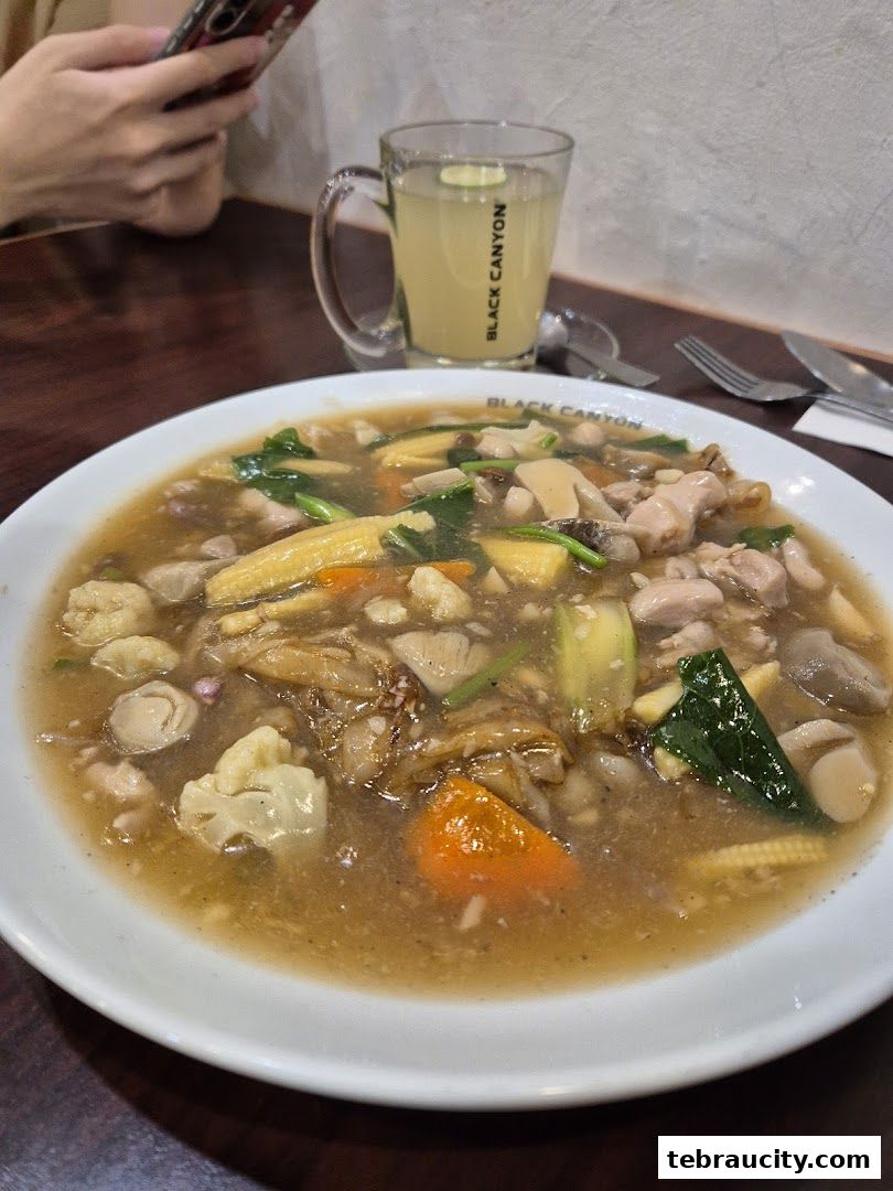 A close-up of a hearty noodle dish with chicken, vegetables, and a refreshing drink.