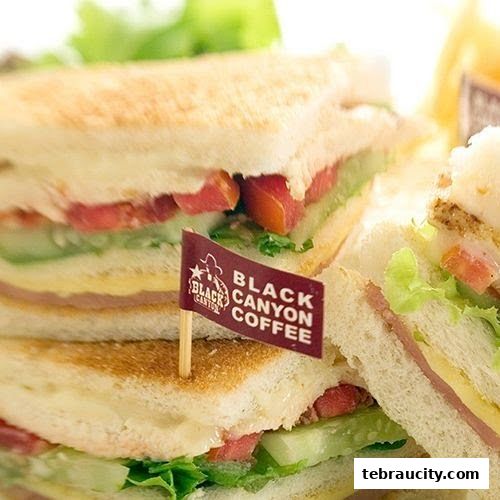 Close-up of stacked sandwiches with fresh ingredients and a Black Canyon Coffee flag.
