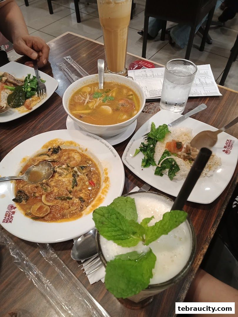 A table at Restoran Black Canyon filled with various dishes and drinks, including soup, rice, and beverages.