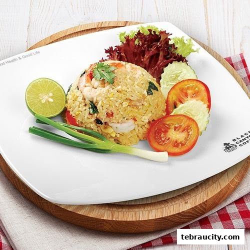 A plate of delicious fried rice with shrimp, garnished with lime, spring onions, tomatoes, and cucumber.