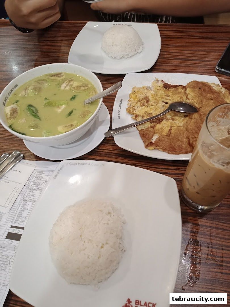A table setting with a bowl of green curry, rice, omelet, and iced coffee.