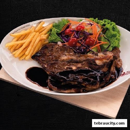 A plate of grilled ribs with fries and a side salad, drizzled with sauce.