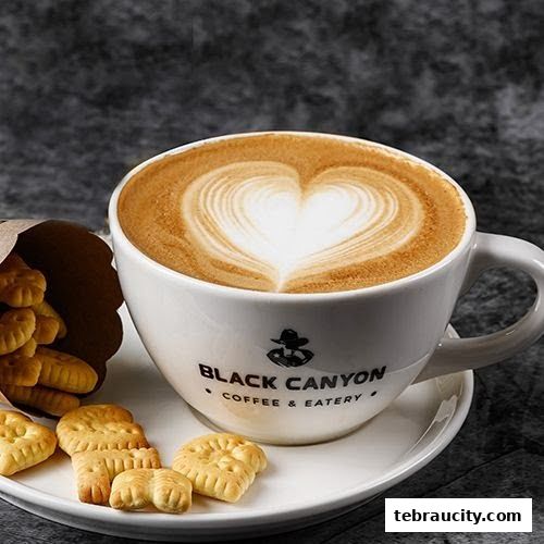 A close-up of a latte with heart-shaped art next to cookies.