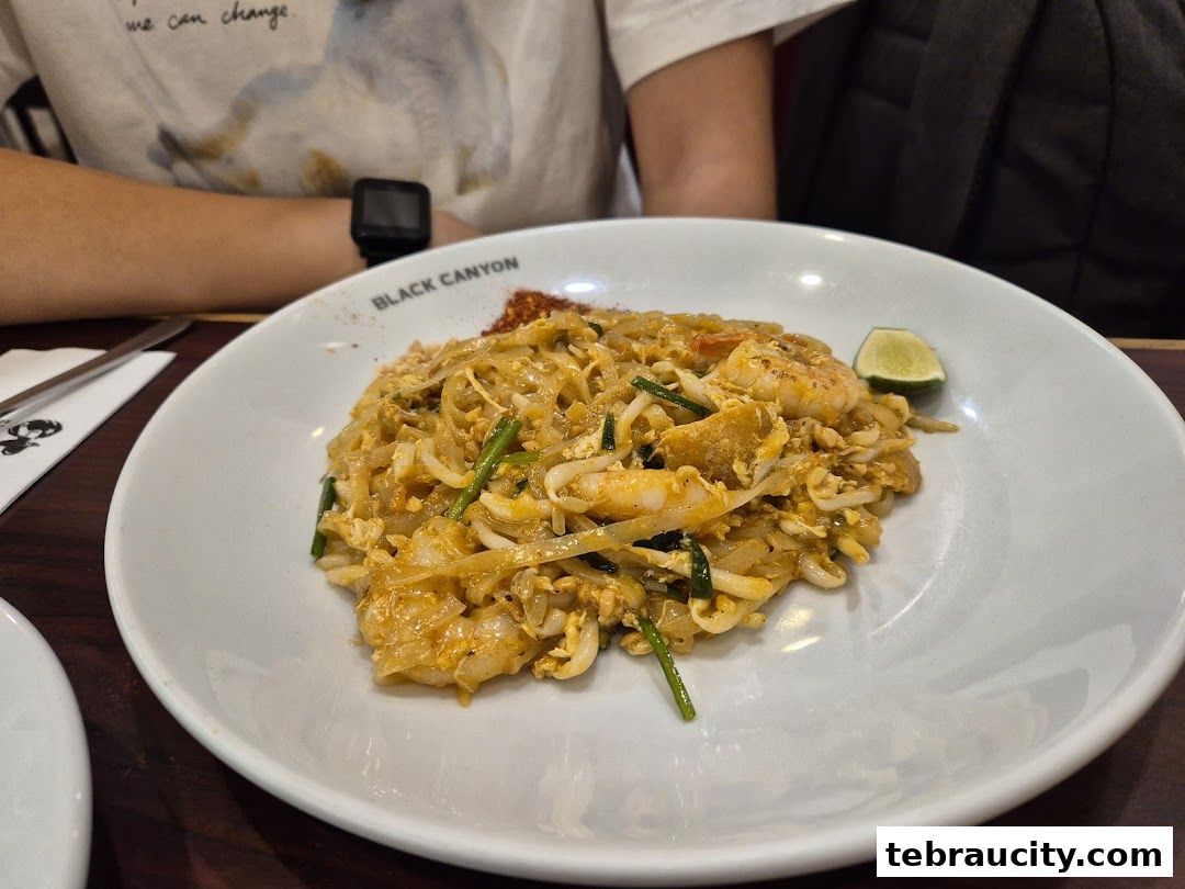 A plate of Pad Thai with shrimp and a lime wedge, served at Restoran Black Canyon.