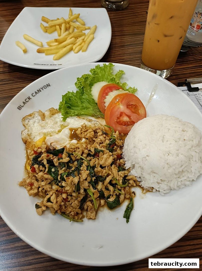 A plate of stir-fried minced chicken with basil, served with rice, a fried egg, and a side of fries.