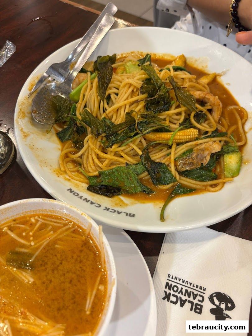 A plate of spaghetti with vegetables and a bowl of soup, with a napkin from Black Canyon Restaurants.