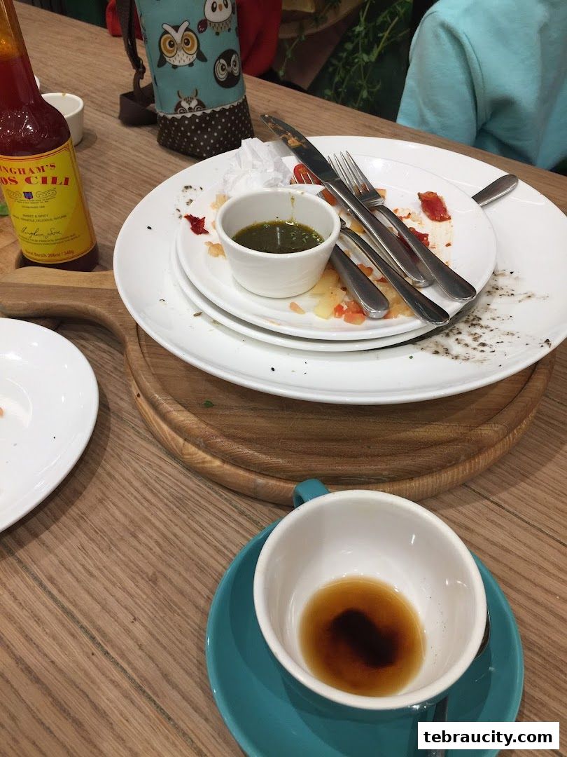 A table setting with used plates, cutlery, a bottle of chili sauce, and a cup of coffee.