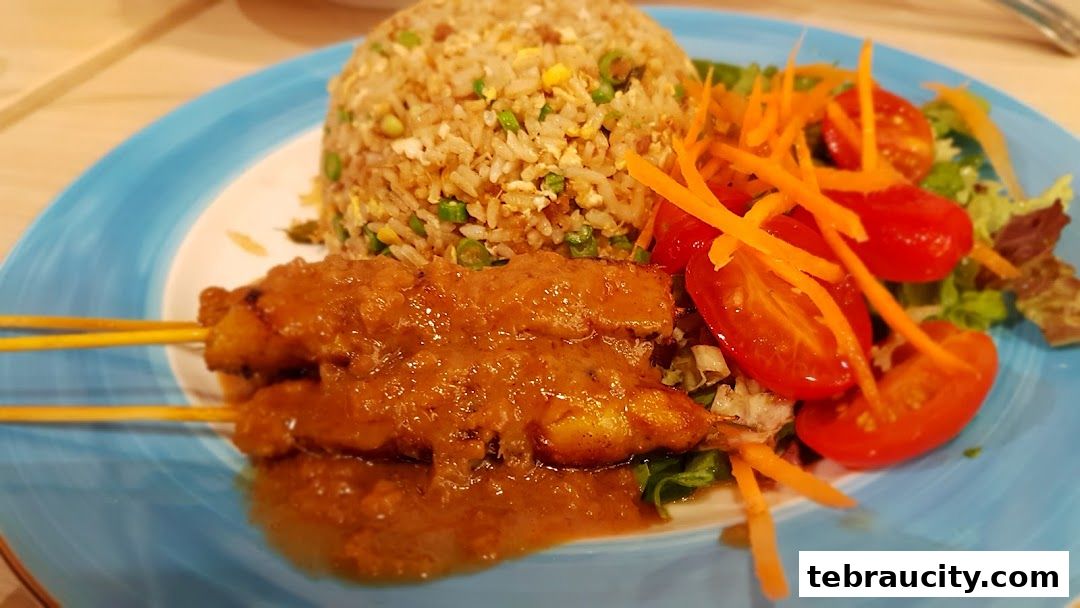 A plate of chicken satay with peanut sauce, fried rice, and a fresh salad.