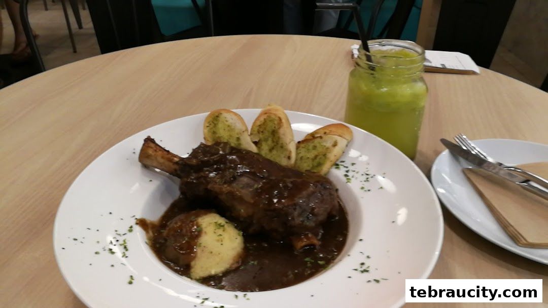 A plate of braised lamb shank with mashed potatoes and garlic bread, served with a green drink.