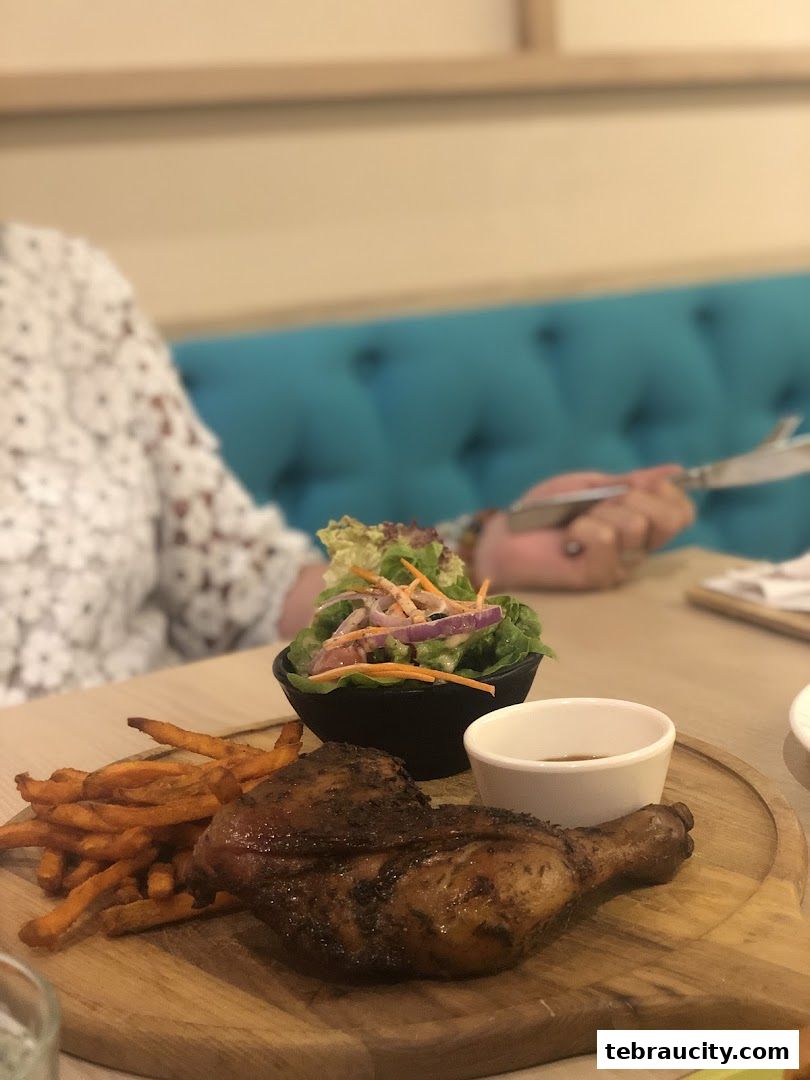 A close-up of a grilled chicken leg quarter with fries and a side salad.