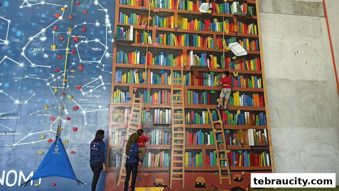 People climbing a colorful indoor rock climbing wall with a bookshelf and constellation theme.