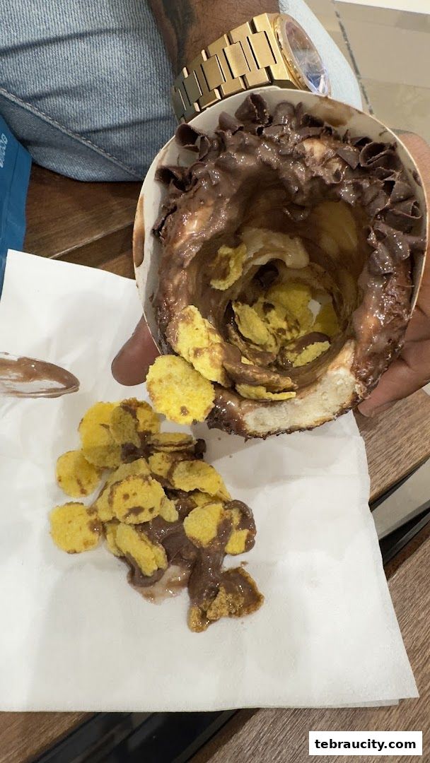 A close-up of a dessert cone filled with chocolate and cornflakes, with some spilling out.