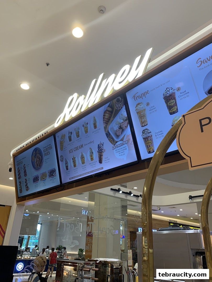 A digital menu board displaying various ice cream and frappe options at Rollney.