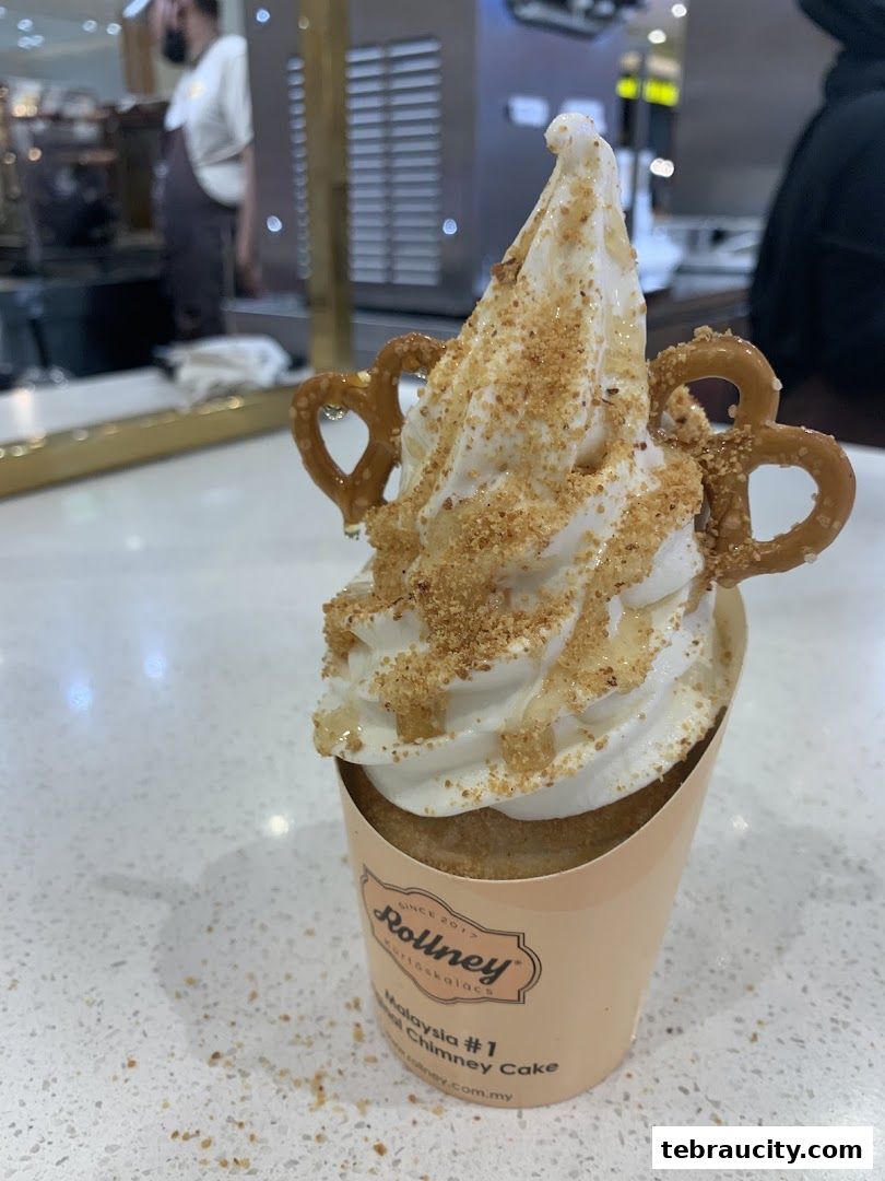A close-up of a soft-serve ice cream cone topped with pretzels and crumble.