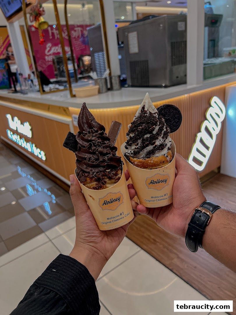 Two chimney cakes with soft serve ice cream and toppings held by two people.