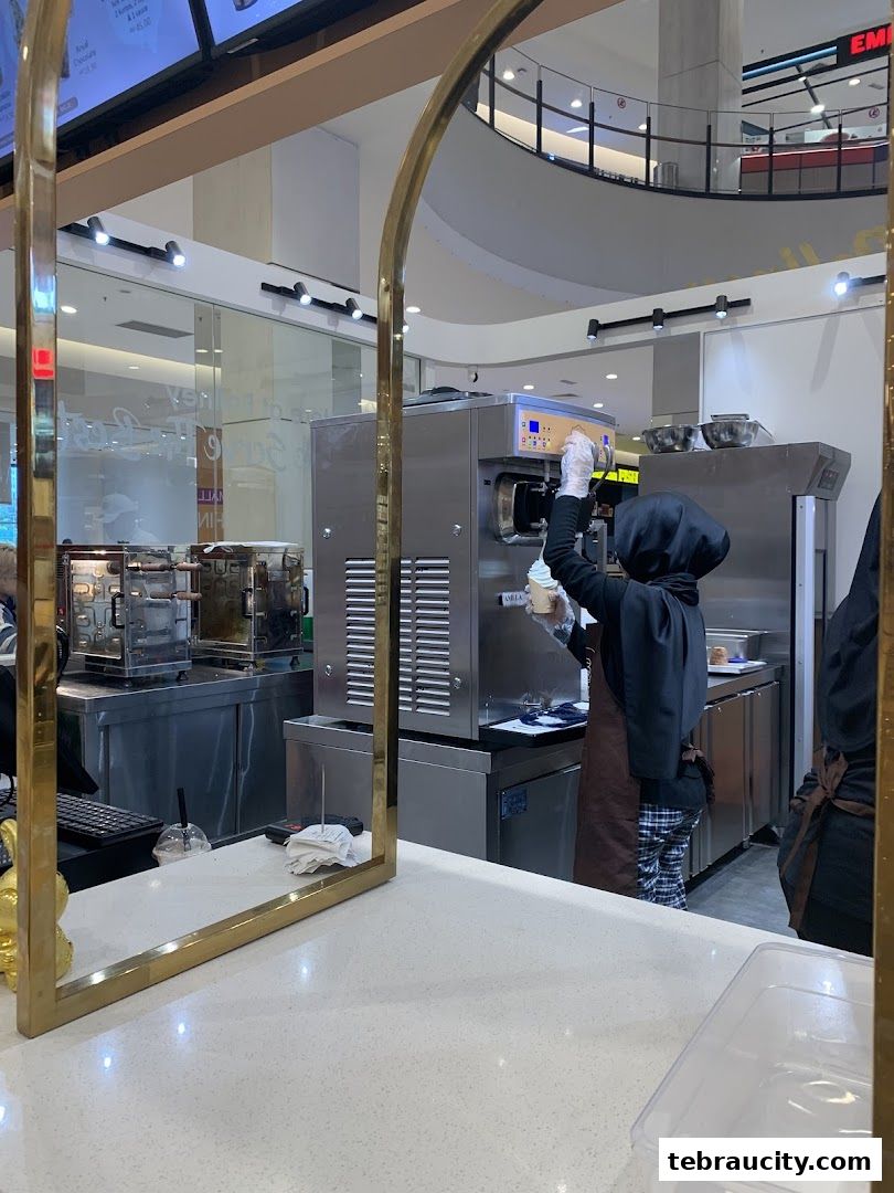 A person in a black hijab and apron making soft serve ice cream at a machine.