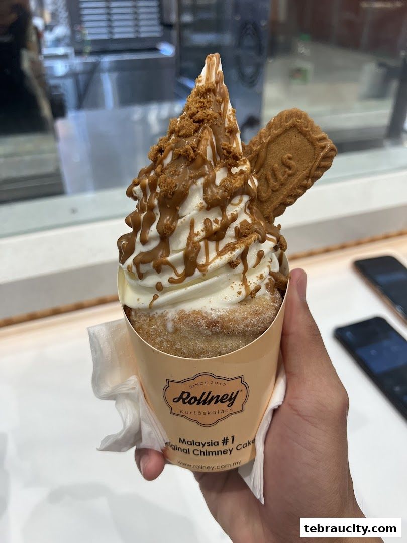 A hand holds a delicious chimney cake topped with soft serve ice cream and Lotus Biscoff.