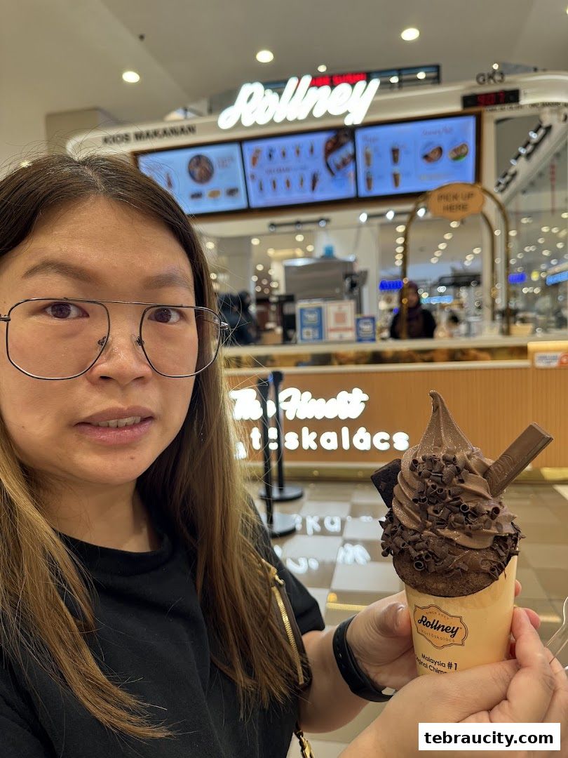 A woman holds a chocolate soft-serve ice cream cone in front of the Rollney shop.