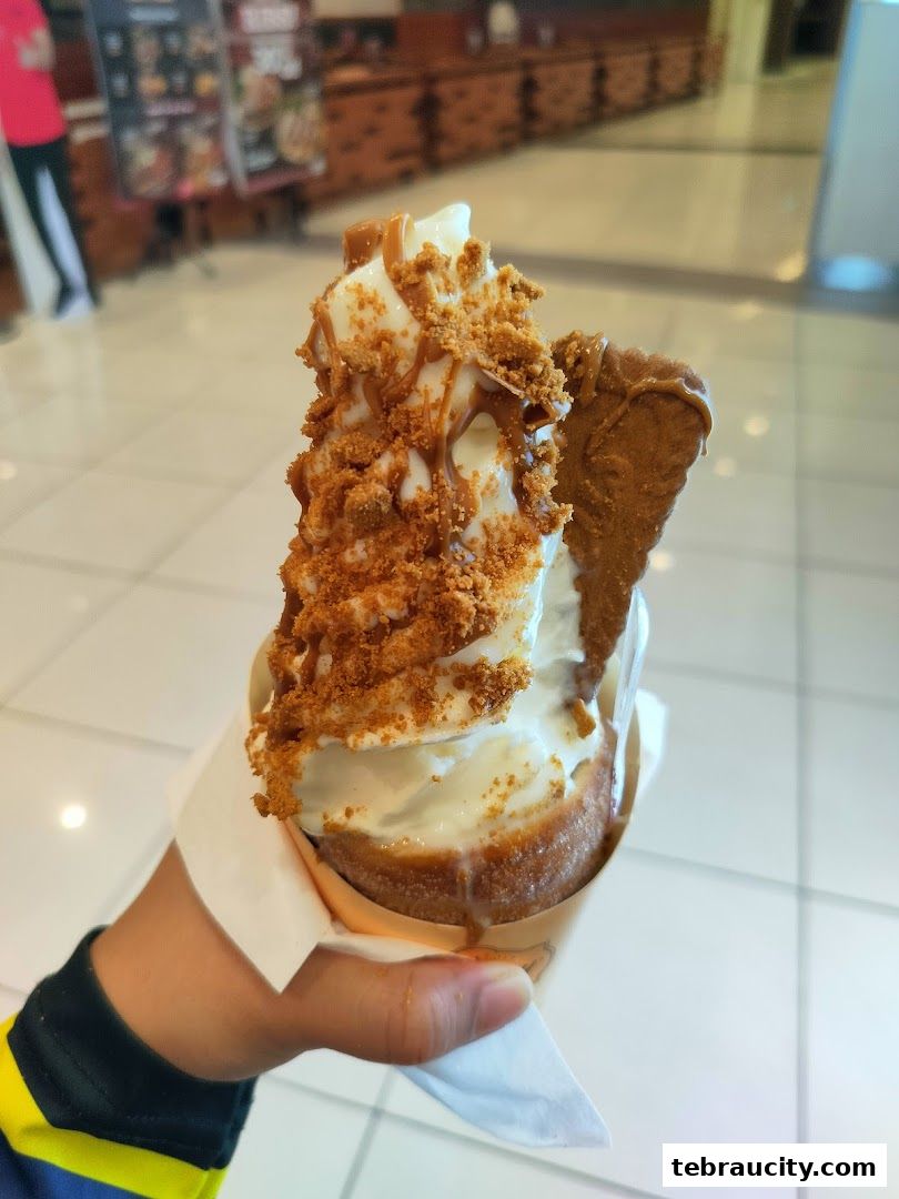 A hand holds a delicious ice cream cone topped with caramel and cookie crumbs.