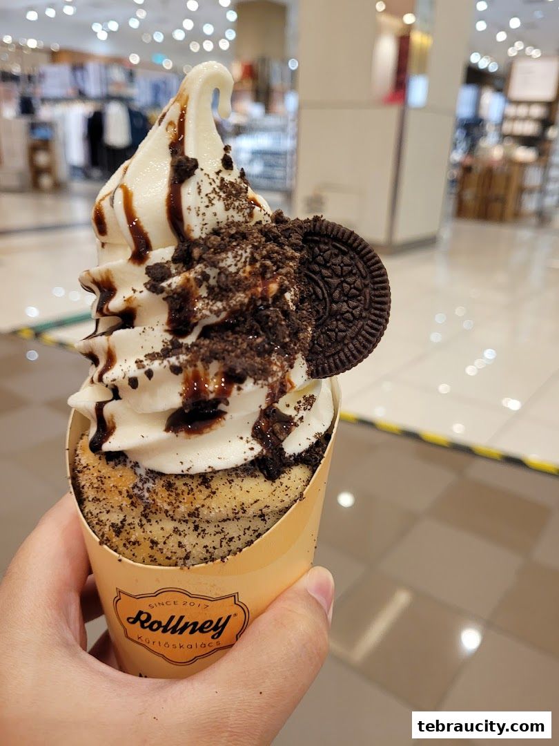 A hand holds a delicious soft-serve ice cream cone topped with chocolate sauce and Oreo cookie crumbles.