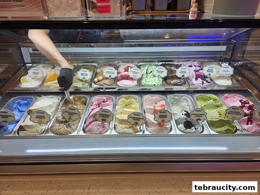 A display case filled with various flavors of ice cream, with a hand scooping one.