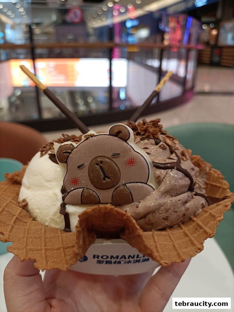 A hand holding a delicious ice cream cone with a cute bear decoration and chocolate sticks.