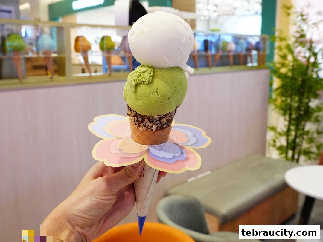 A hand holds a triple-scoop ice cream cone with green and white ice cream.