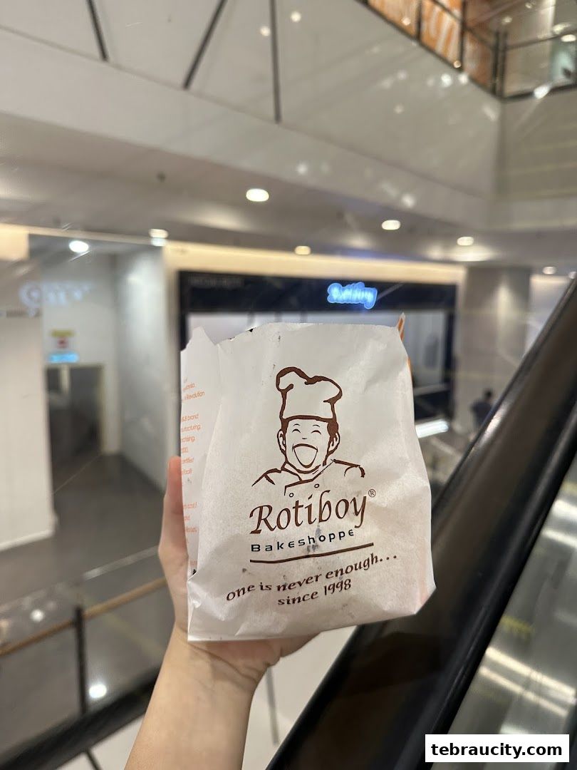 A hand holds a Rotiboy paper bag with the brand logo and slogan.