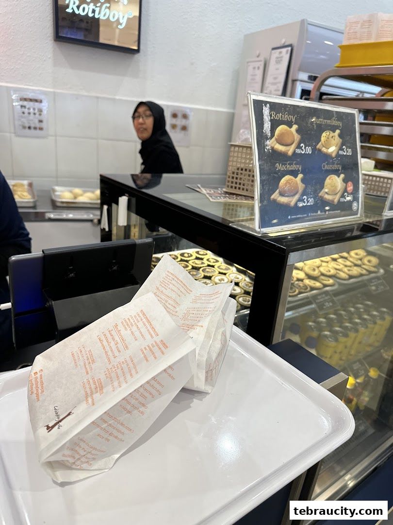 A tray with paper bags from Rotiboy, with a menu board and baked goods visible.